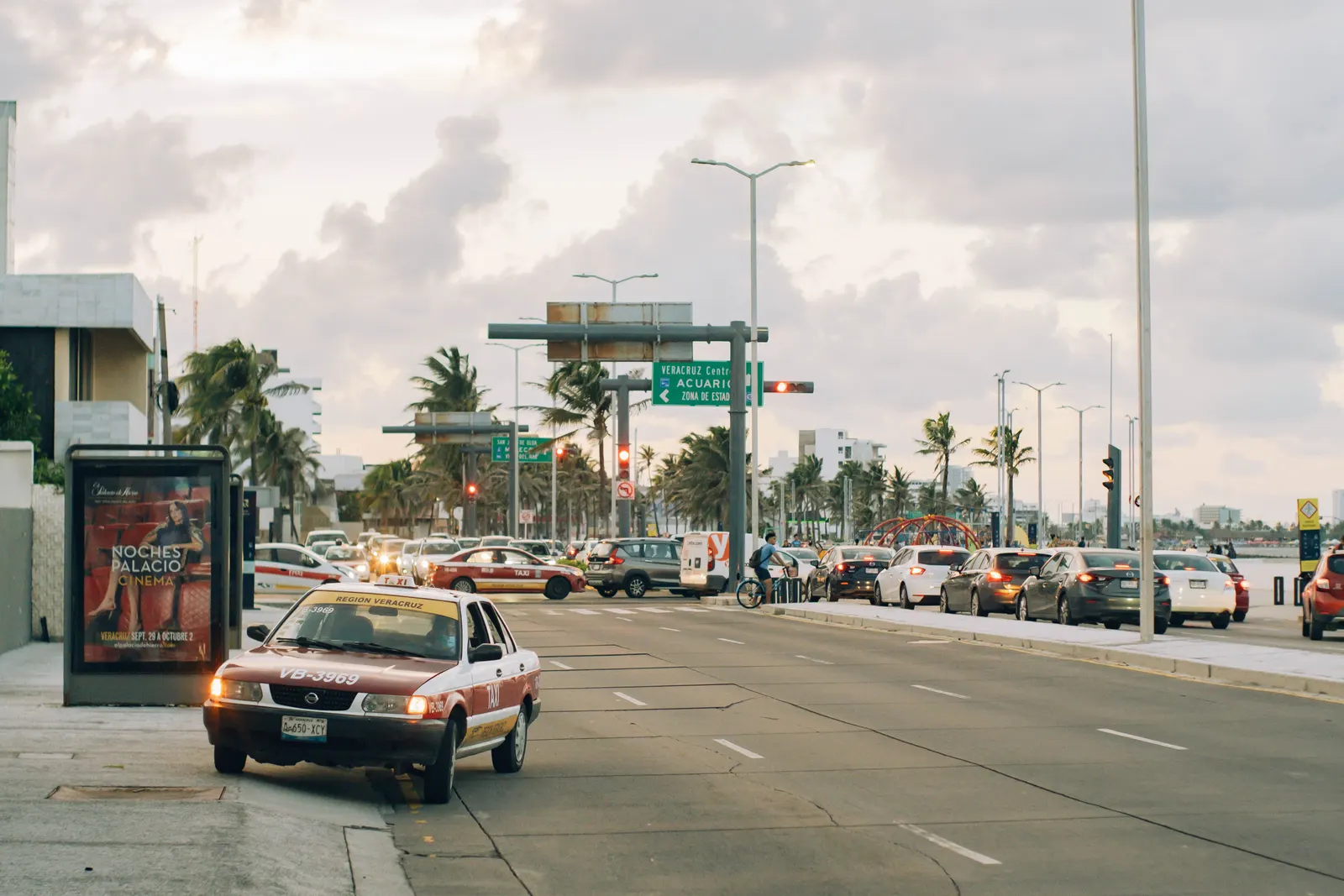 Traffic flows along a bustling street in Veracruz, Mexico, with palm trees and urban scenery at dusk.
