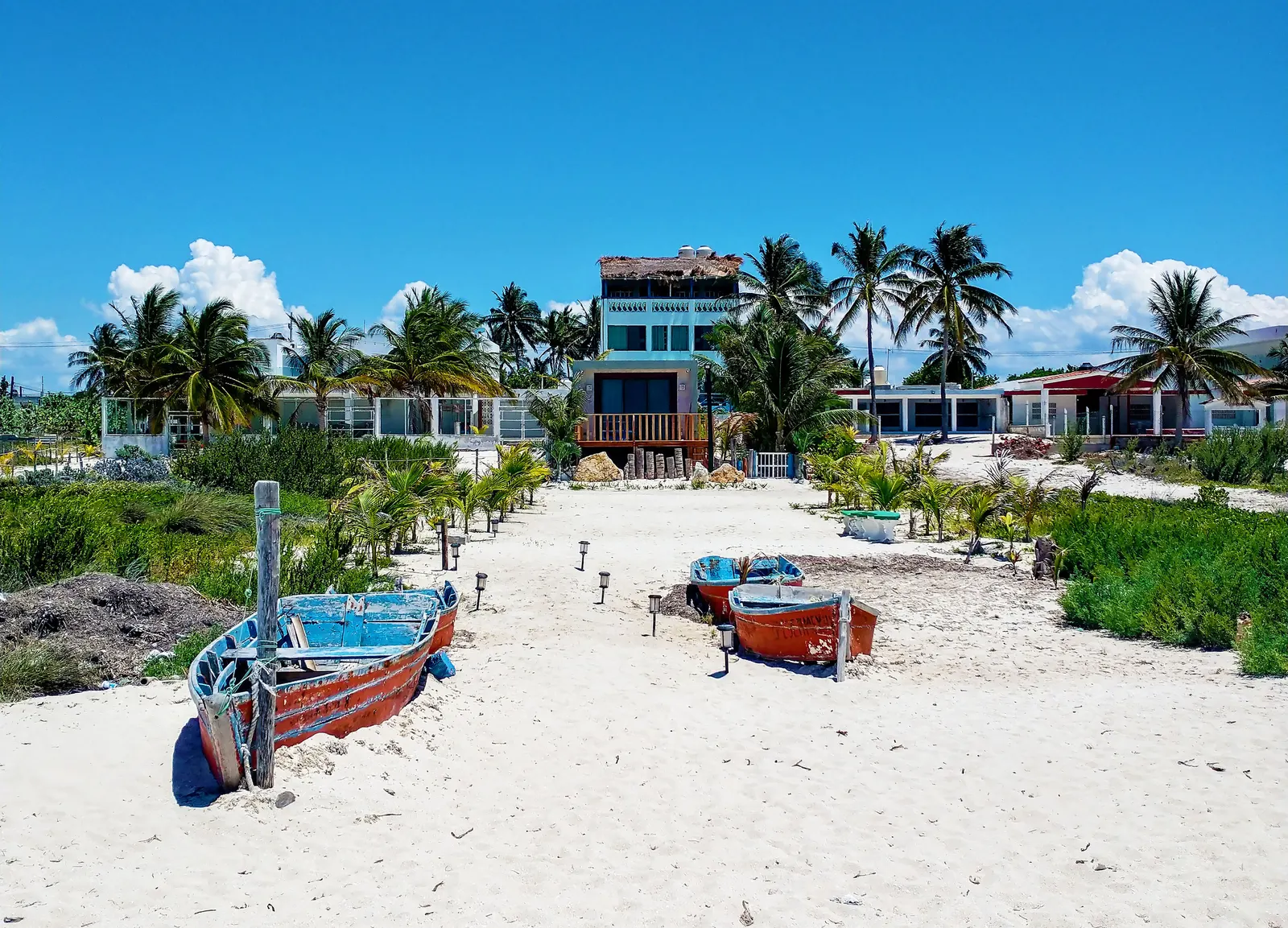 A tranquil tropical beach in Progreso, Yucatan, featuring boats and coconut palms under a bright blue sky.