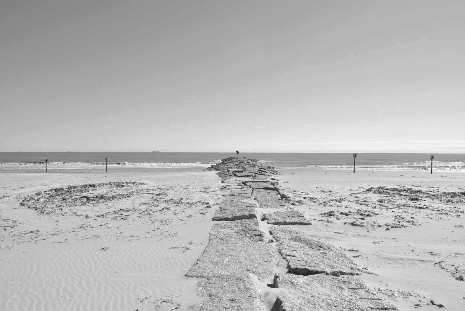 Monochrome view of a stone walkway leading to the ocean at Galveston, TX beach.